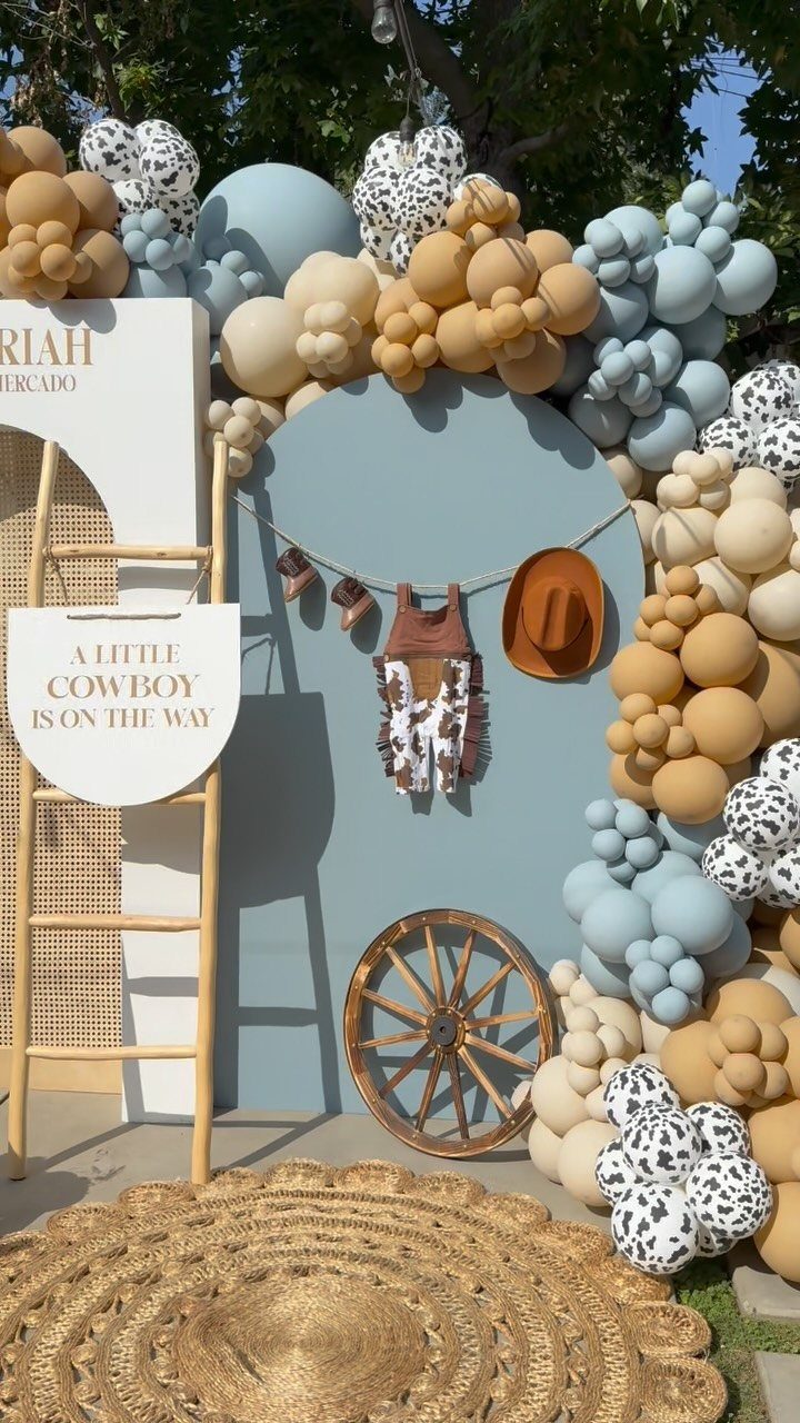 Cowboy themed baby shower decor with balloons, wagon wheel, and baby western clothes.