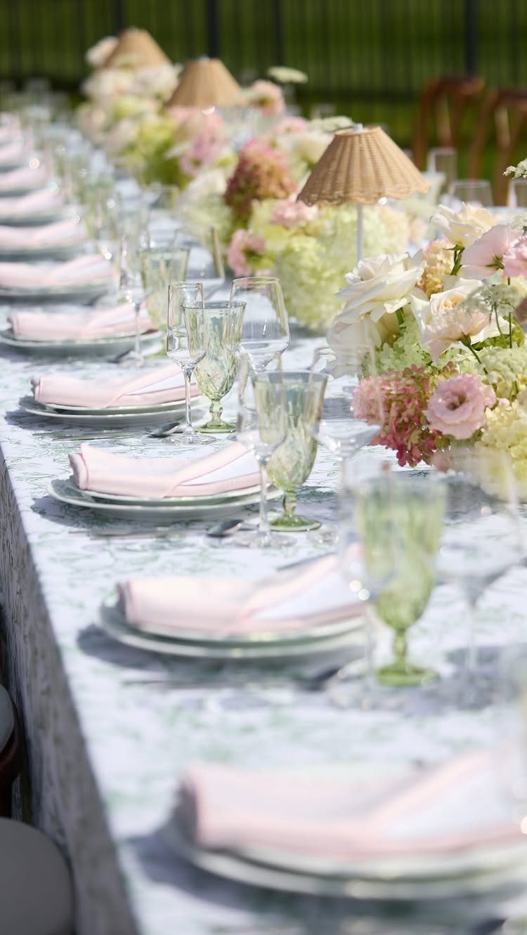 Long outdoor table set with pink napkins and lush white and pink floral centerpieces.