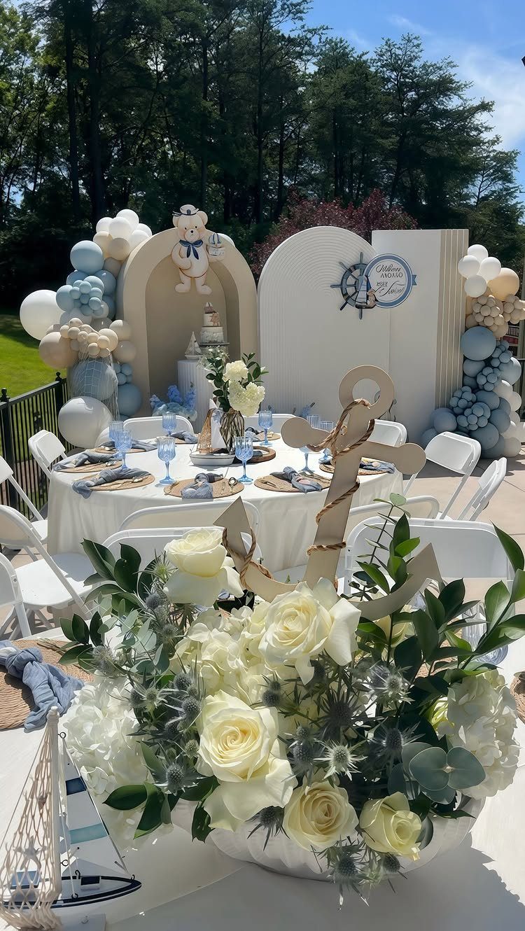 Nautical baby shower table setting with white roses, gold anchor, and blue balloons.