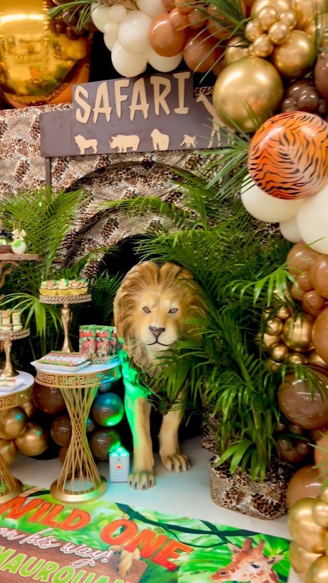 Safari party setup with a lion statue, tropical leaves, and gold balloons.