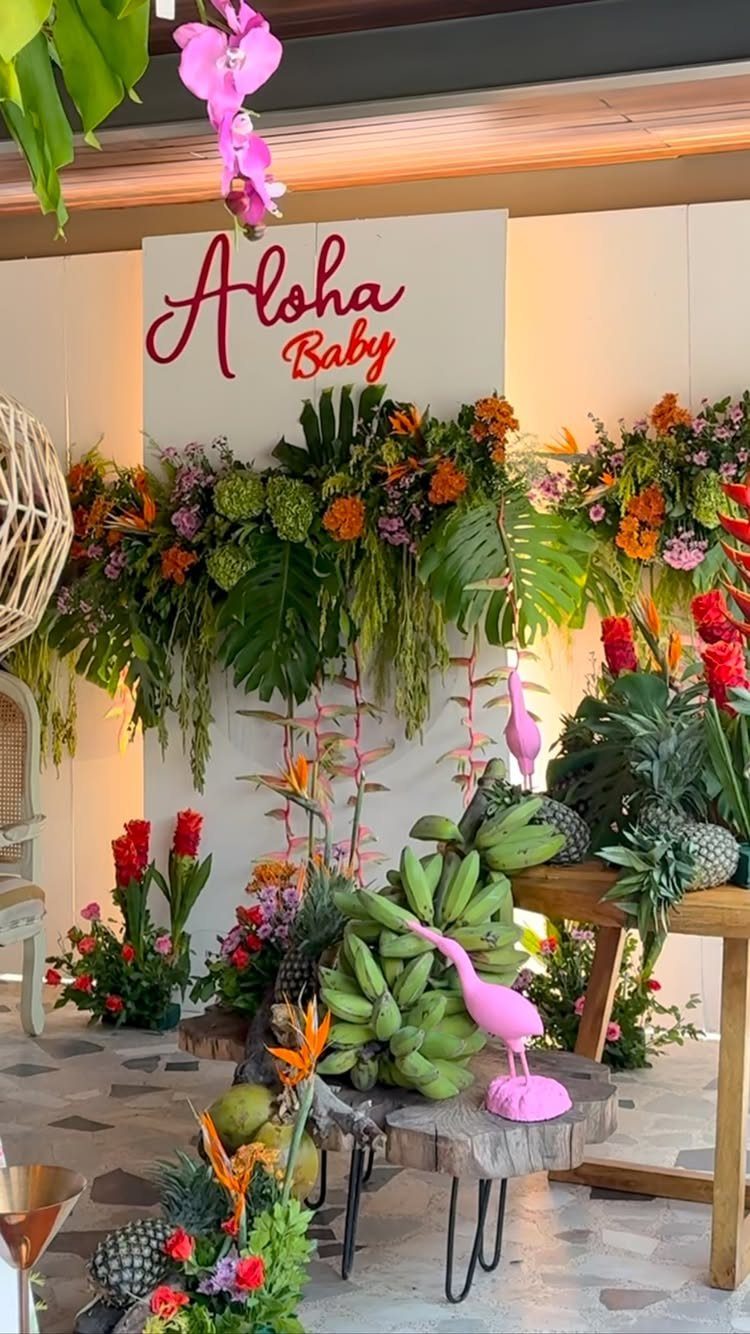 Tropical baby shower decor with Aloha Baby sign, exotic flowers, and fresh fruit.