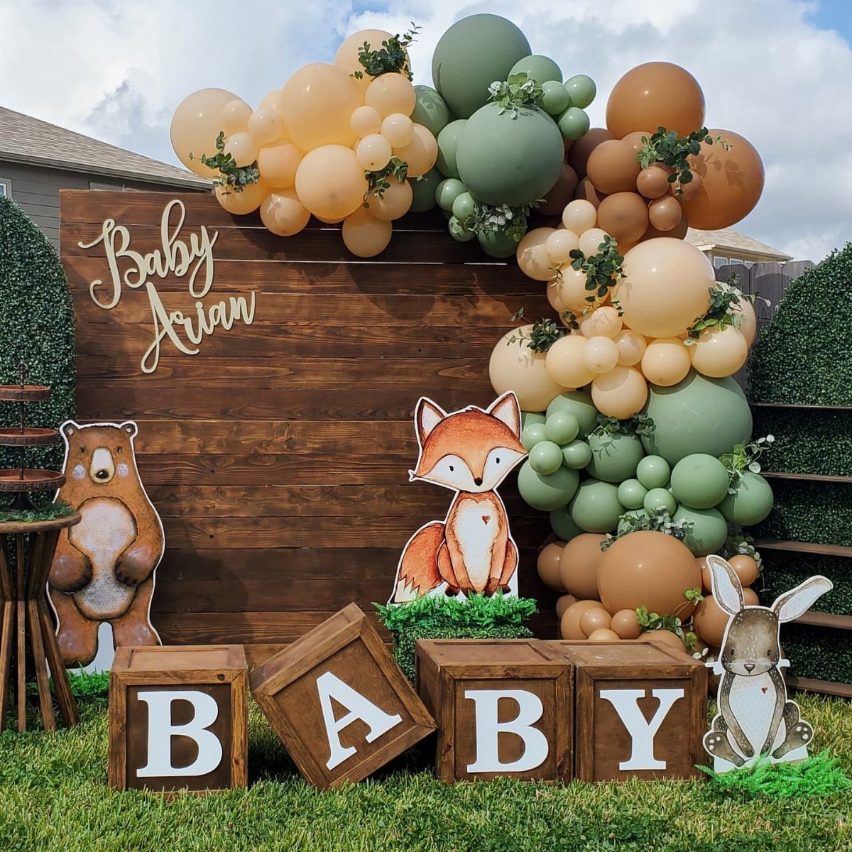 Woodland themed baby shower backdrop with forest animal cutouts and earth-toned balloons.