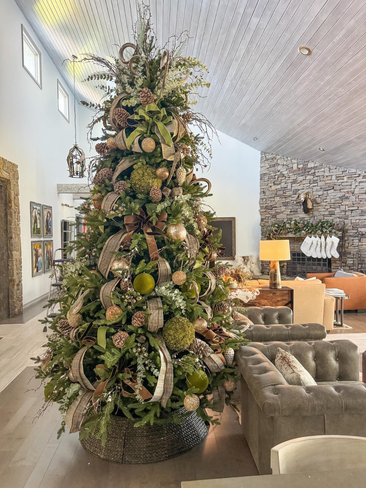 Decorated Christmas tree with pinecones, gold ornaments, and brown ribbons in a living room.