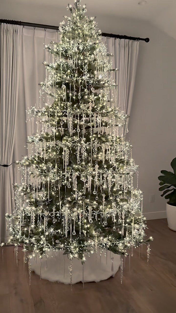 Tall Christmas tree decorated with white lights and silver icicle ornaments in a room.