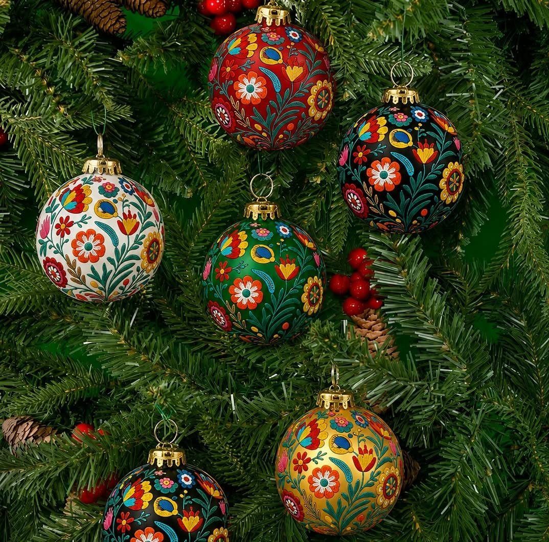 Colorful floral painted ornaments hanging on a green Christmas tree with red berries.