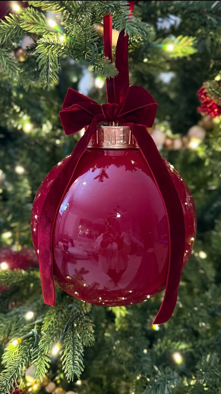 Large red glossy Christmas ornament with a velvet bow on a lit tree
