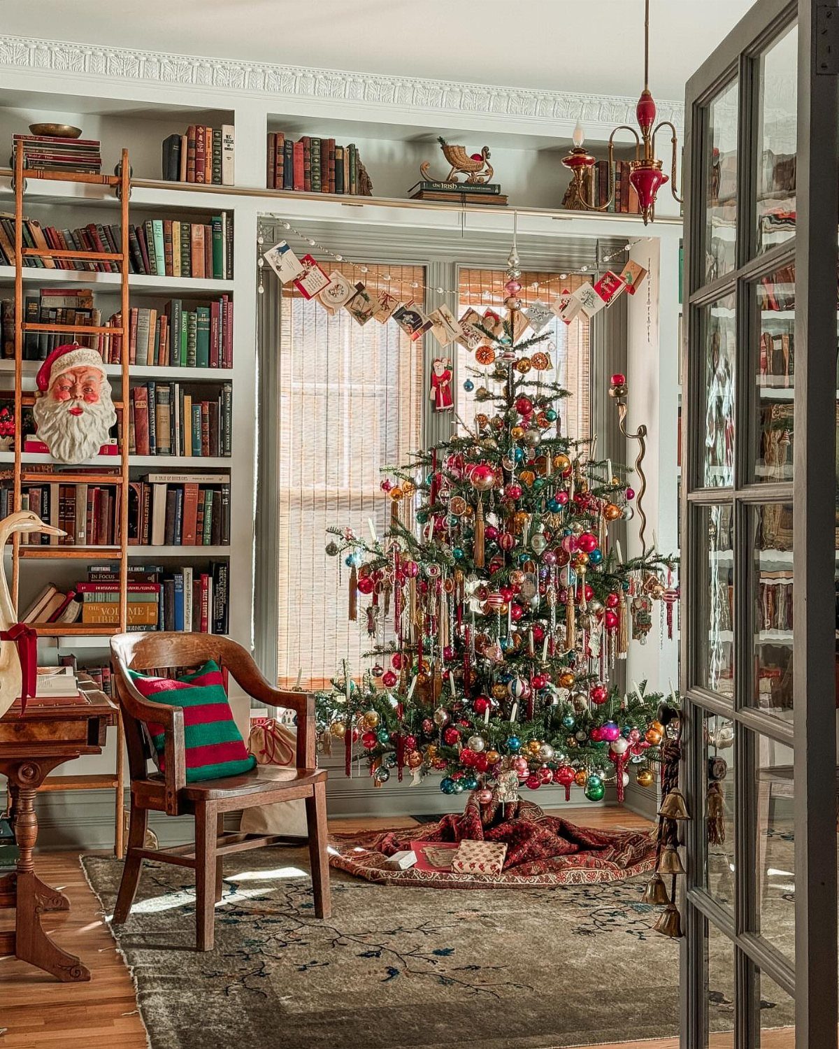 Decorated Christmas tree with colorful ornaments and tinsel in a cozy library room.