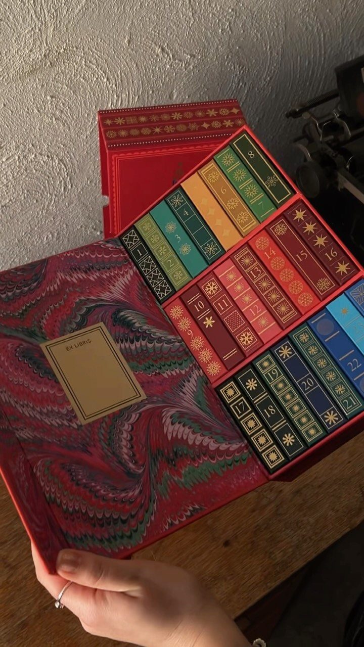 Red book-style advent calendar with colorful numbered drawers held by a hand.