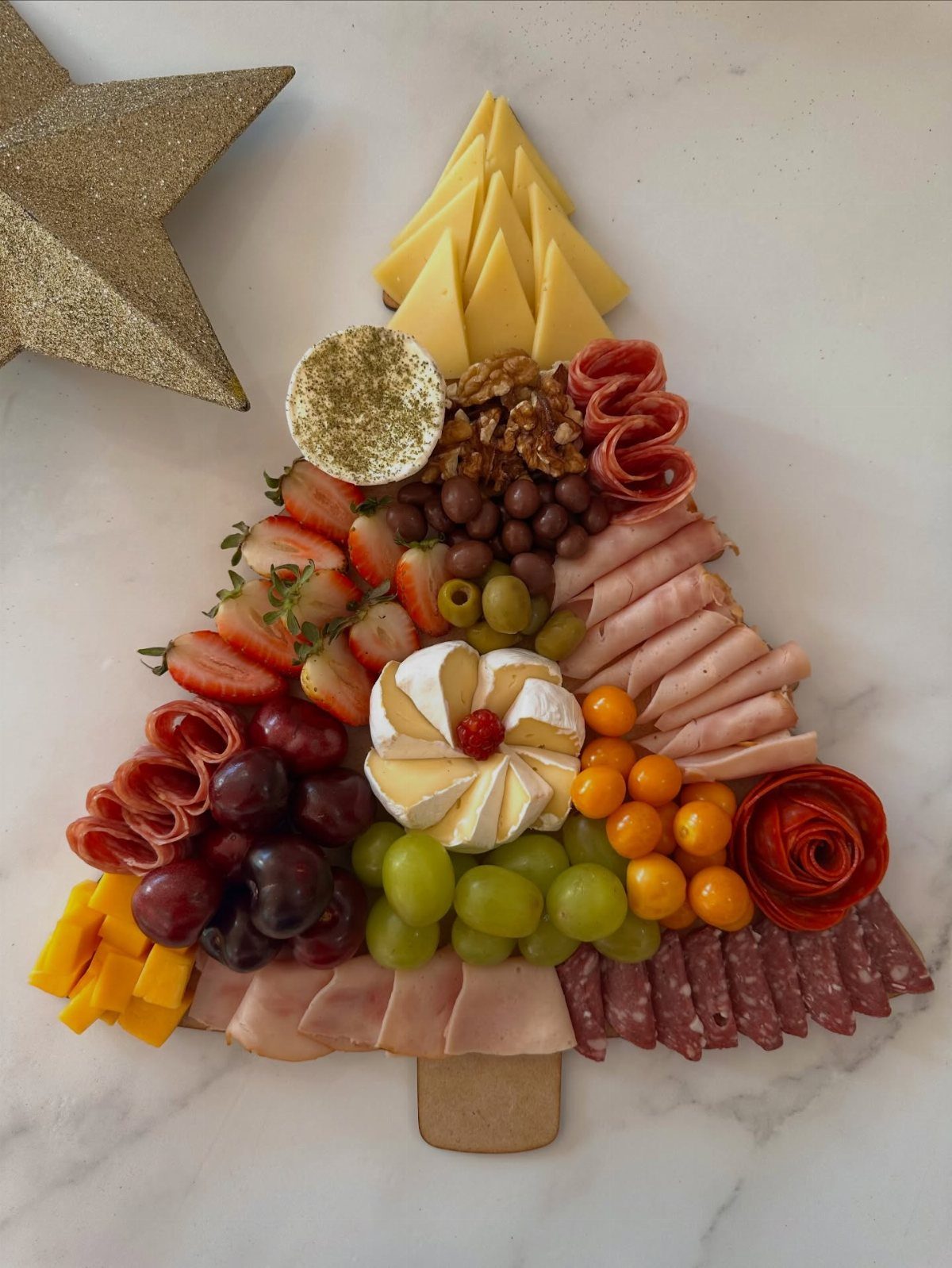 Christmas tree shaped charcuterie board with meats, cheeses, and fruits on marble surface