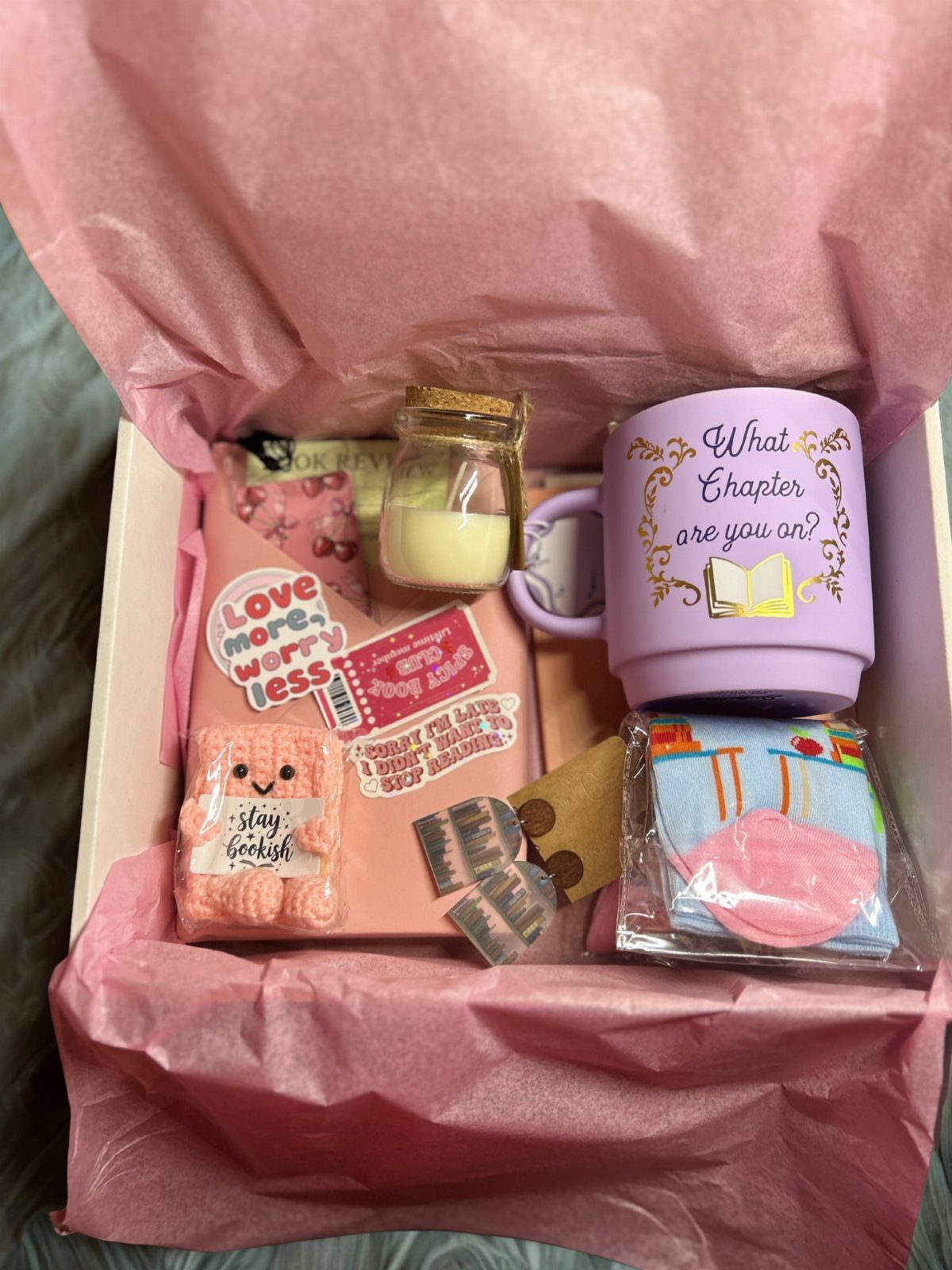 Gift box with a pink book, purple mug, candle, and cozy accessories.