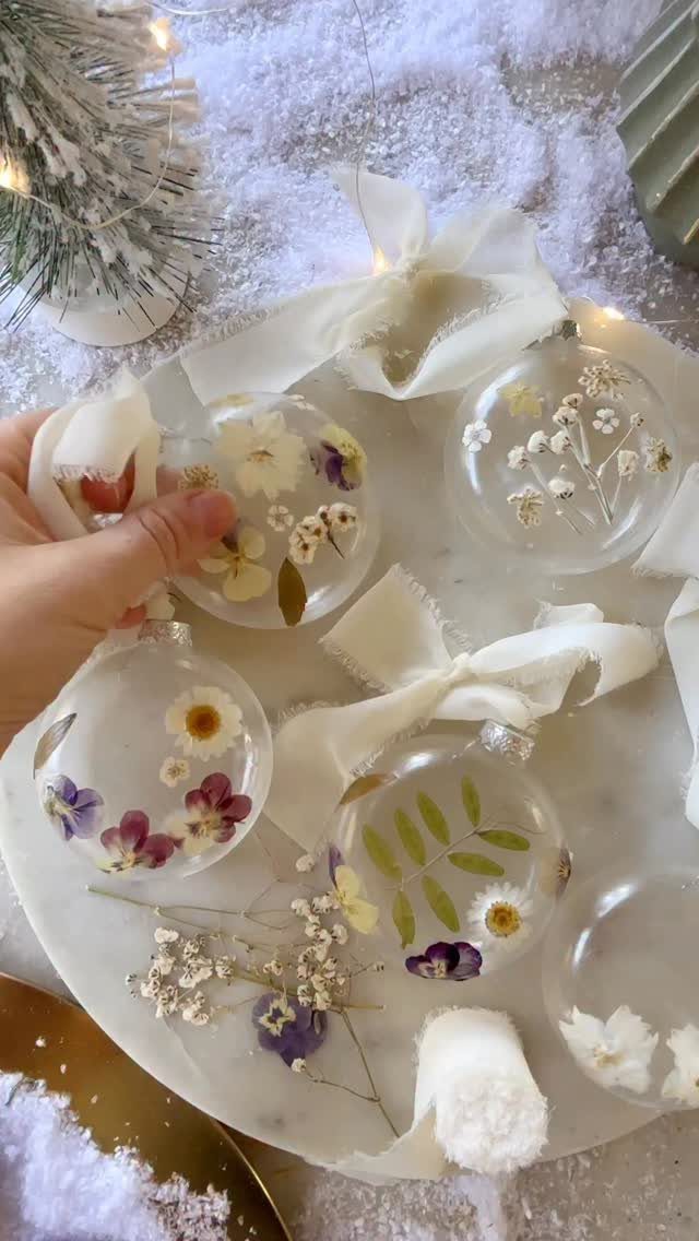 Clear glass Christmas ornaments filled with dried flowers on a snowy marble surface.