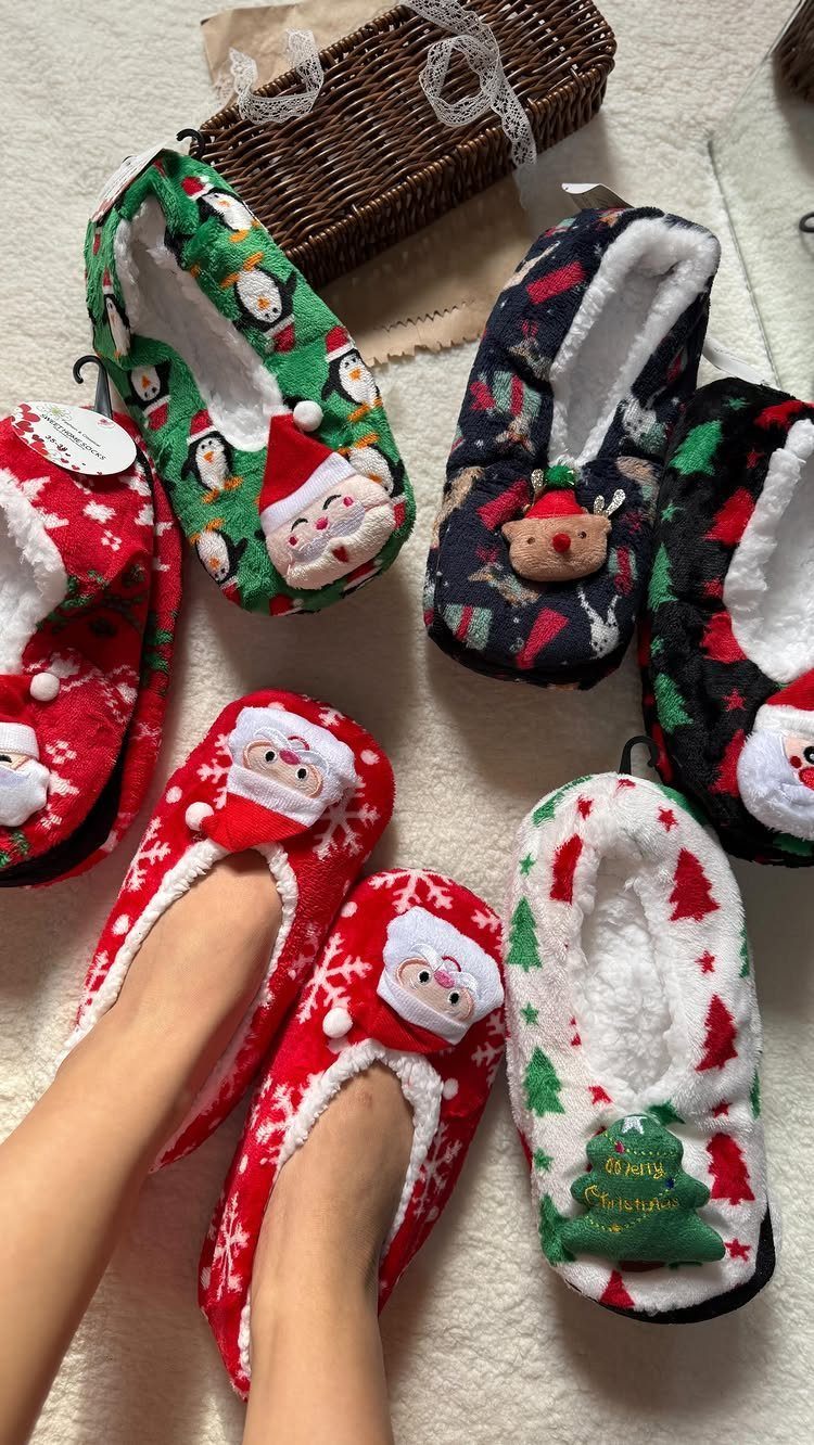 Christmas-themed plush slippers with Santa and reindeer designs on a white carpet.