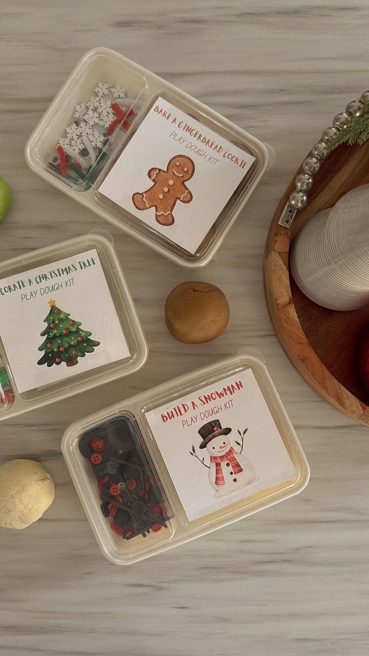 Three Christmas themed play dough kits in plastic containers on a marble surface.