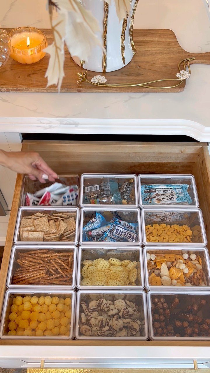 Clear acrylic storage bins organizing various snacks inside a wooden kitchen drawer.