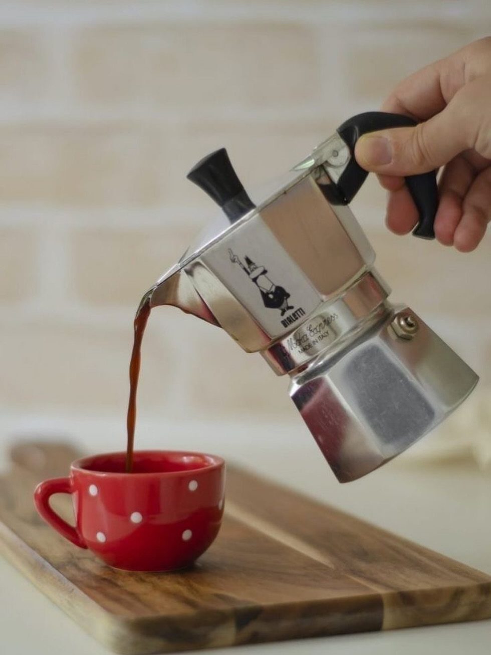 Bialetti Moka Express coffee maker pouring espresso into a red polka dot cup