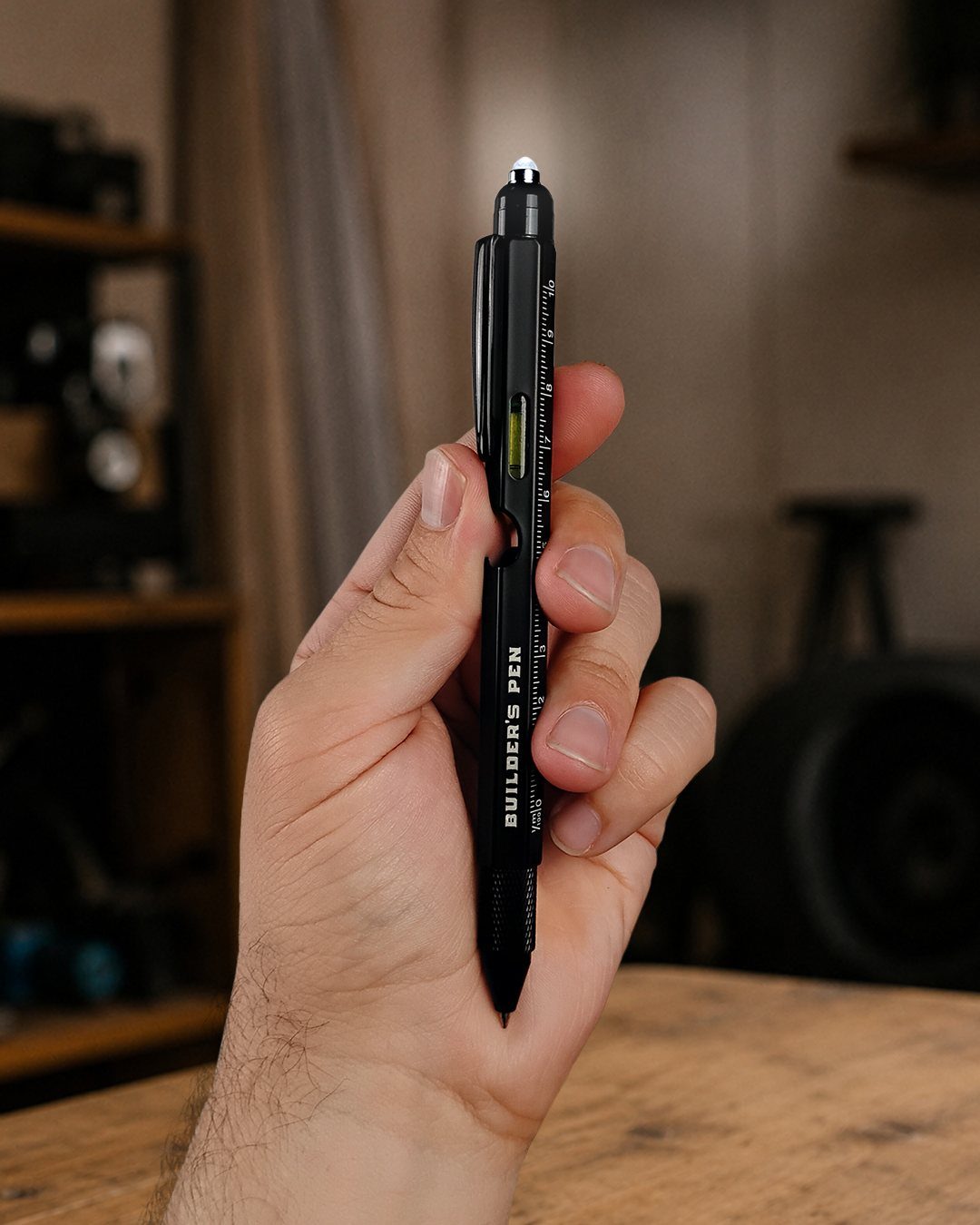 Black multitool pen with ruler and level held in a person's hand.