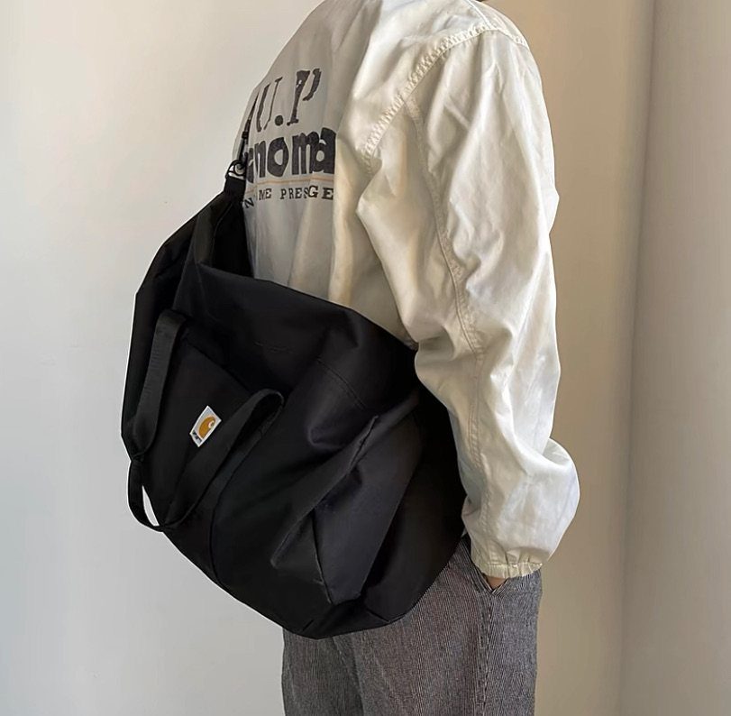 Black Carhartt messenger bag worn by a person in a white shirt.