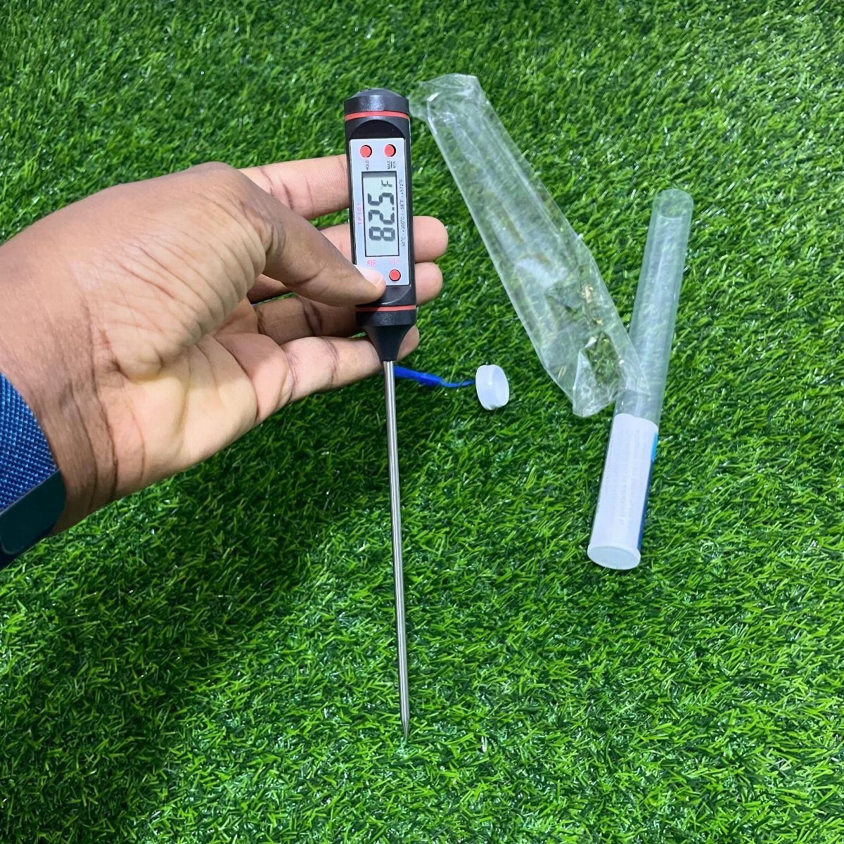 Digital meat thermometer held by a hand over green artificial grass surface