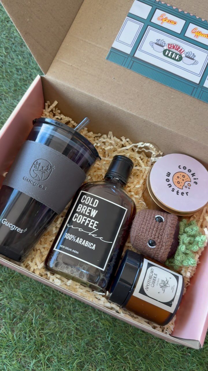 Gift box containing cold brew coffee, a black tumbler, and sweet treats on grass.