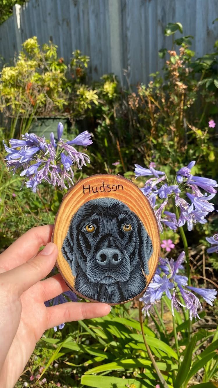 Hand-painted black dog portrait on a wooden slice held in a sunny garden