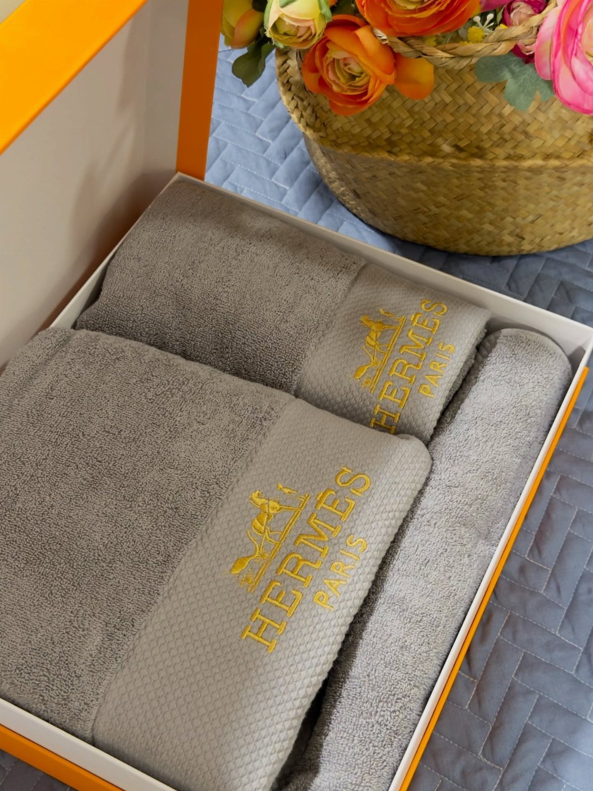 Grey luxury towels with gold logos in an orange gift box with flowers.