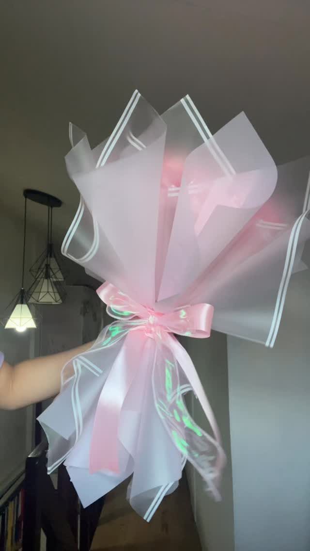 Glowing pink light bouquet wrapped in white and pink translucent paper with ribbon.