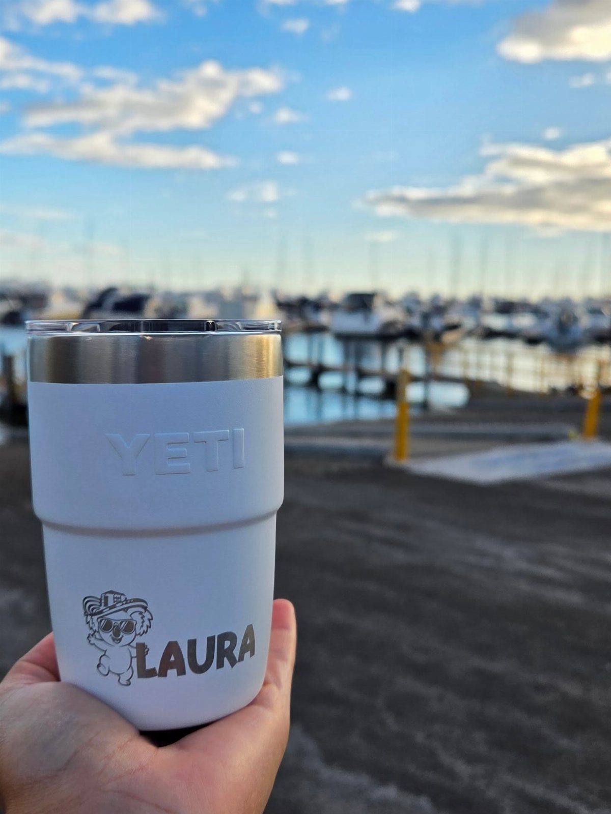 White personalized Yeti mug with name Laura held against a blurred marina background.