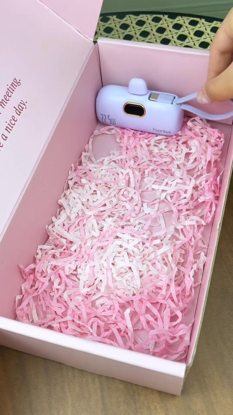 Purple portable charger resting on pink shredded paper inside a pink gift box.