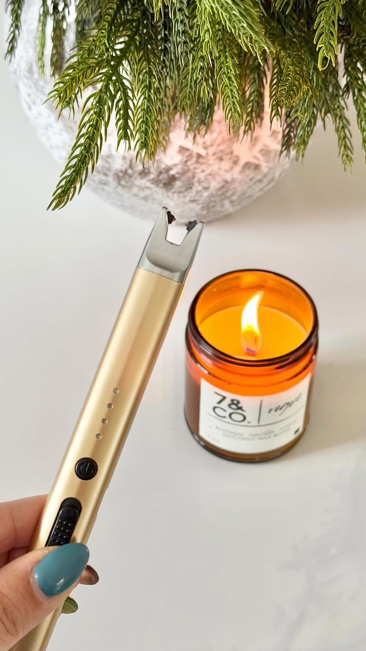 Gold electric arc lighter held next to a lit amber glass candle jar.