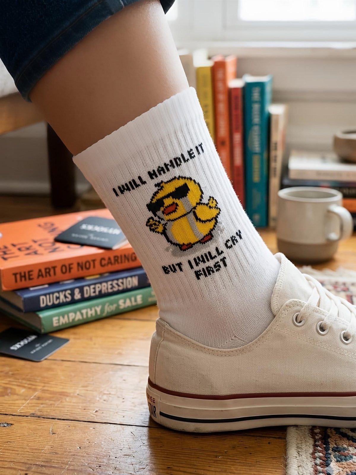 White crew sock with a yellow duck and funny text worn with sneakers.