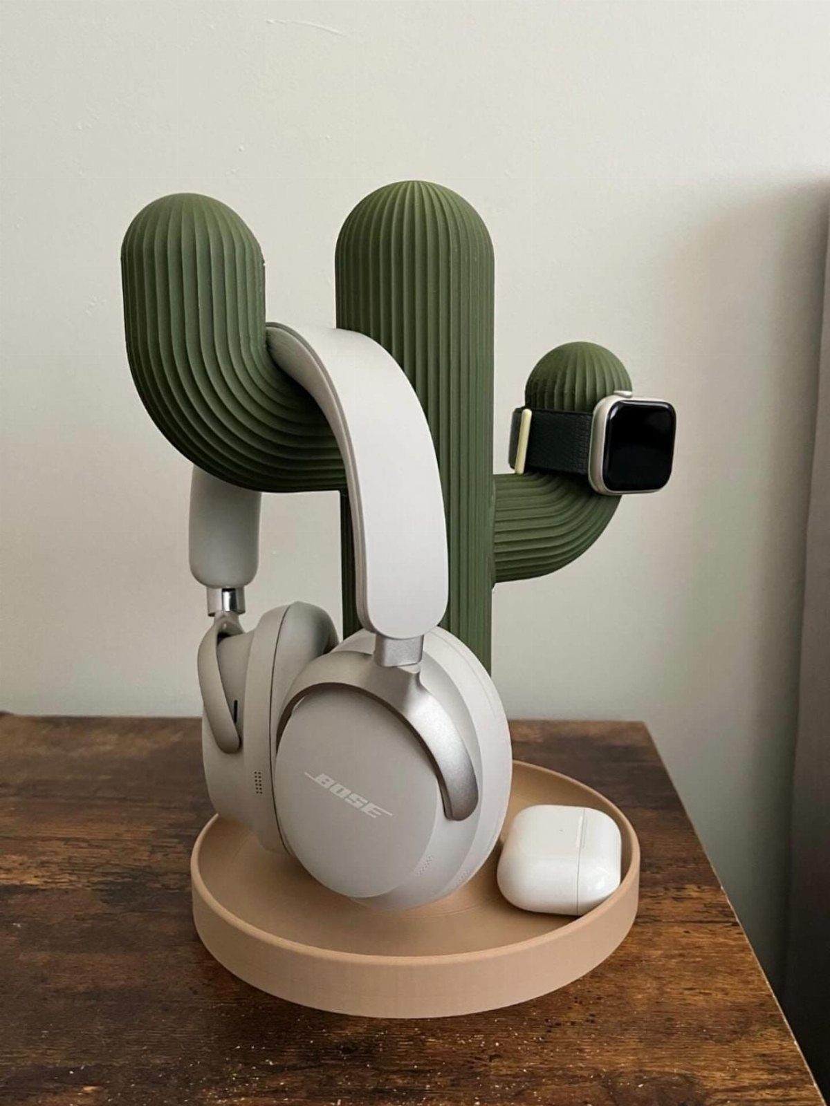 Cactus-shaped headphone stand holding white headphones, a smartwatch, and wireless earbuds.