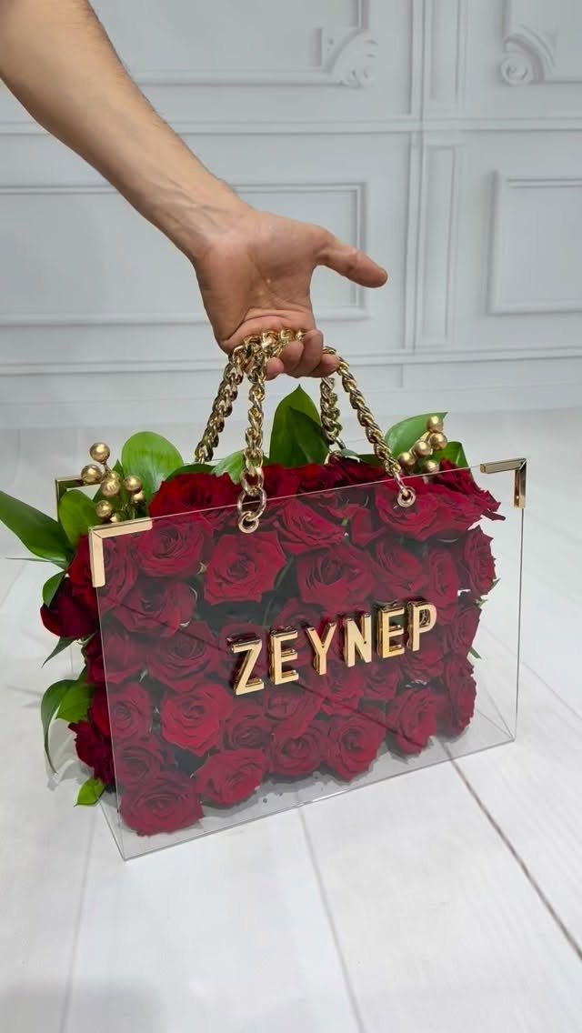 Acrylic handbag filled with red roses and gold lettering held by a hand