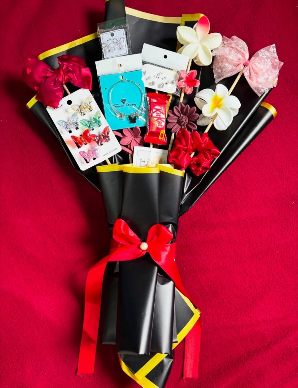 Gift bouquet with jewelry, hair bows, and artificial flowers wrapped in black paper.