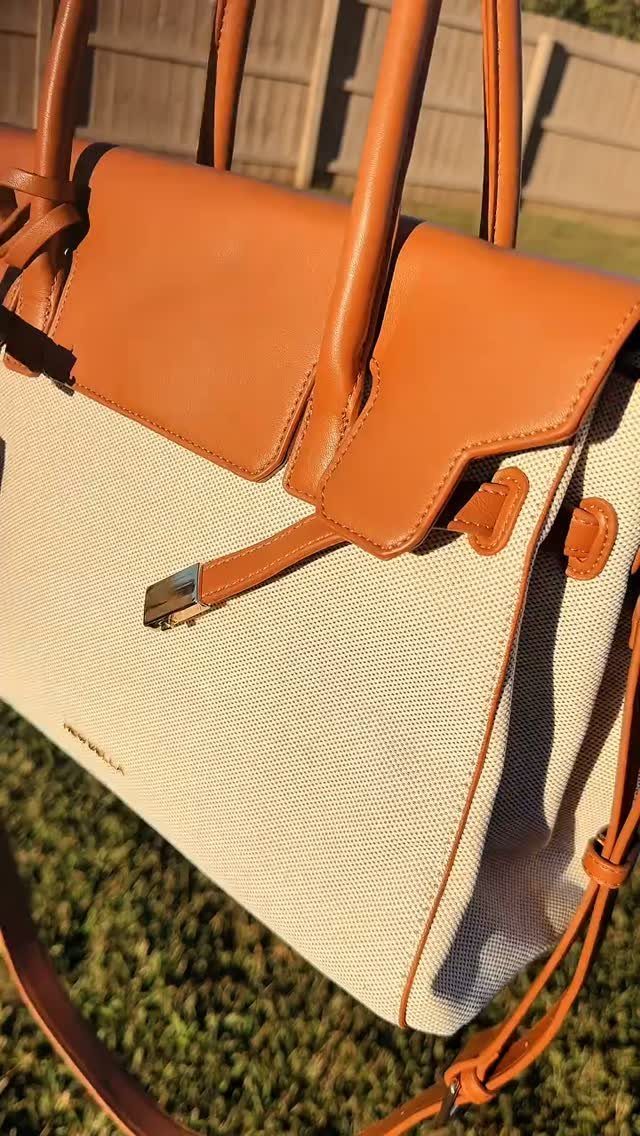 Cream canvas tote bag with tan leather handles and trim on green grass.