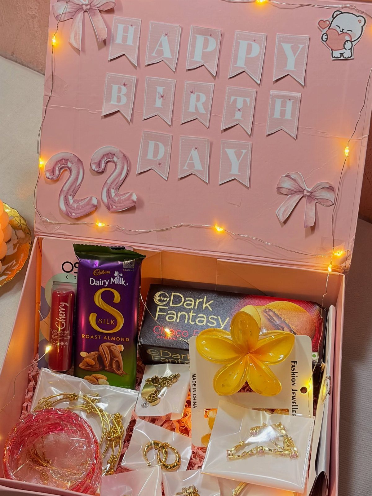 Pink birthday gift box with chocolates, jewelry, and fairy lights for a 22nd birthday.