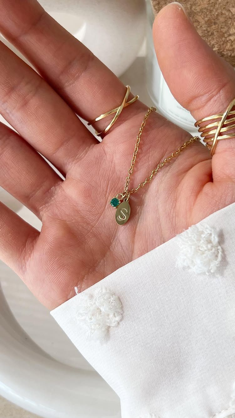 Gold necklace with a green birthstone and letter S charm held in a hand