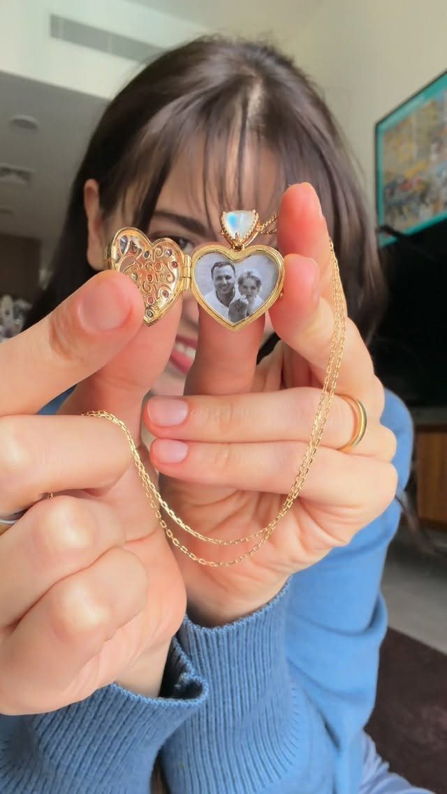 Gold heart-shaped locket necklace held open to show a photo of a couple.