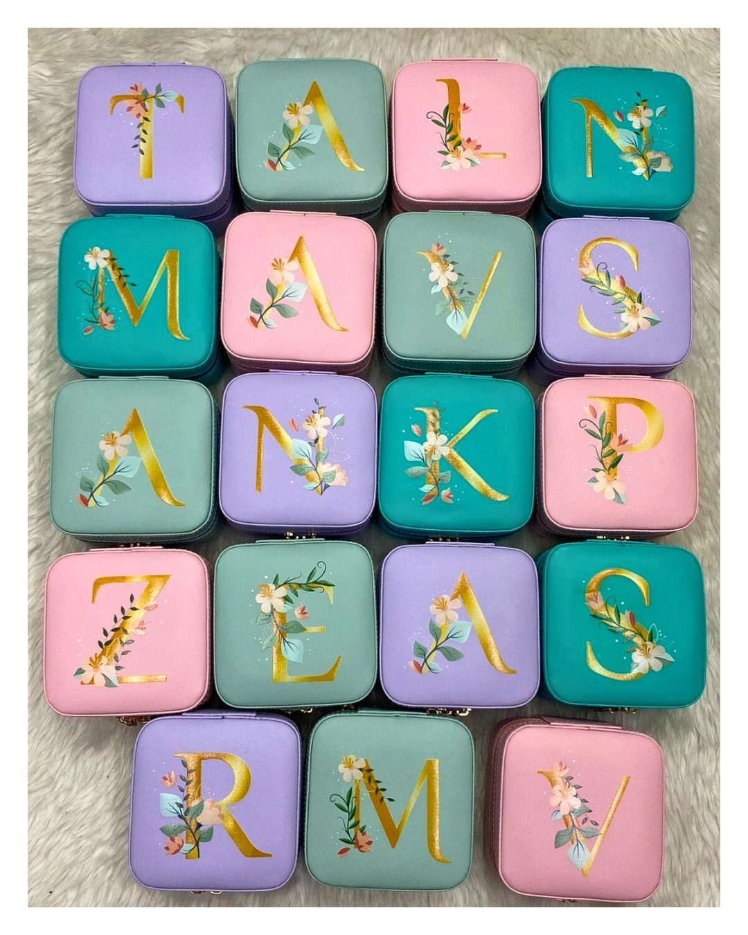 Small square personalized jewelry cases in pastel colors with gold floral initials.