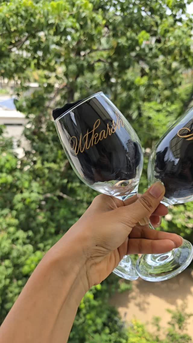 Hand holding two wine glasses, one featuring gold cursive personalized name text.