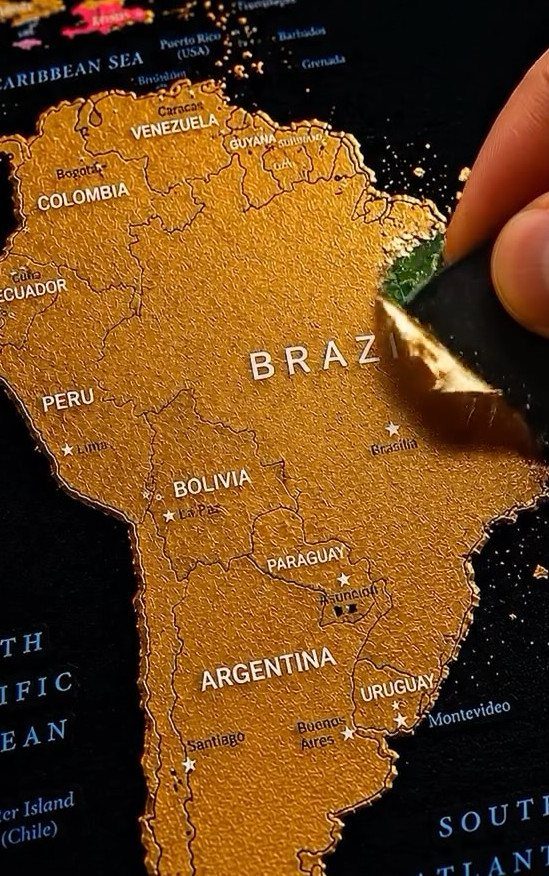 Gold scratch-off world map of South America being scratched to reveal green colors.