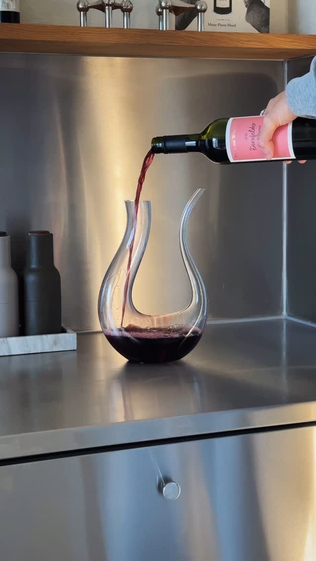 Red wine being poured from a bottle into a curved glass decanter