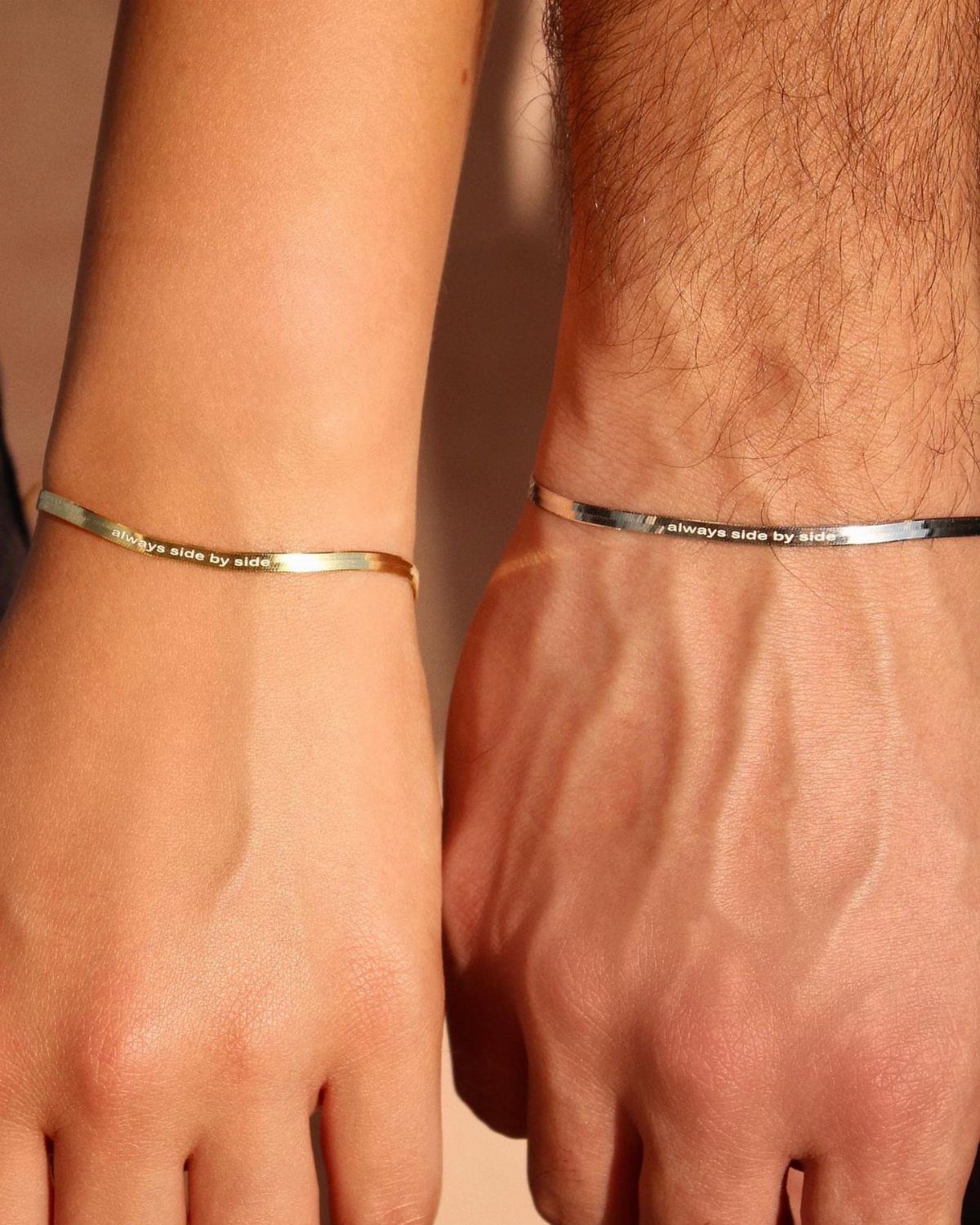 Two wrists wearing matching gold and silver engraved cuff bracelets side by side.
