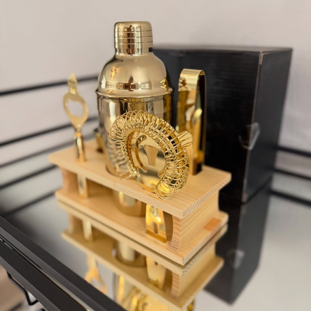 Gold cocktail shaker set on a wooden stand with a black gift box