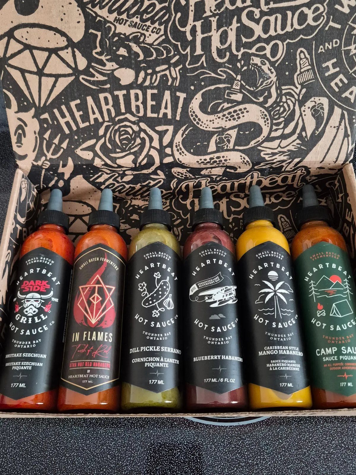 Six colorful bottles of gourmet hot sauce arranged inside a branded gift box.