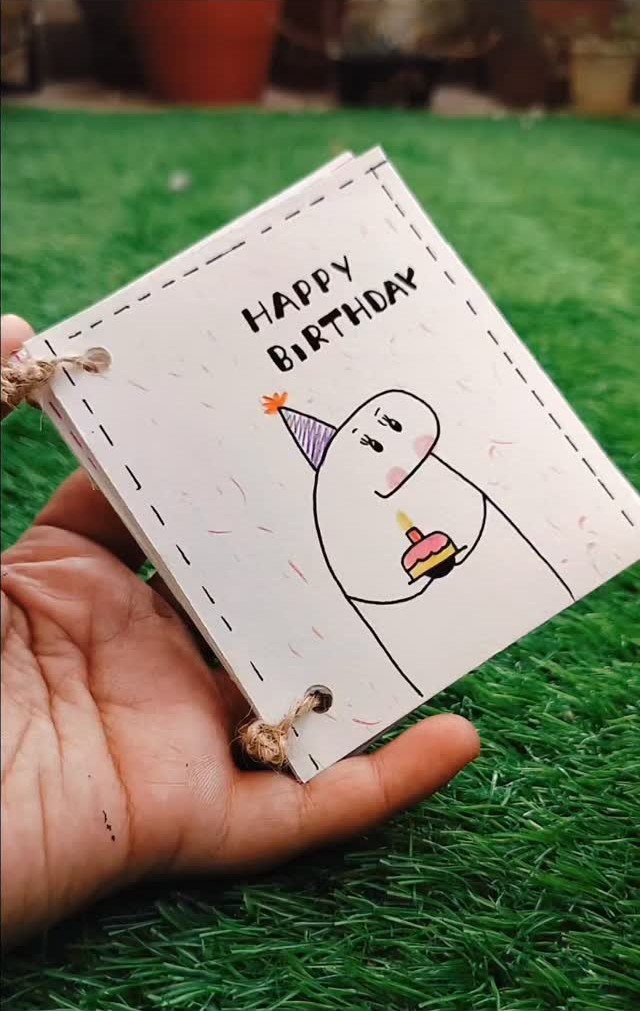 Handmade birthday card with a cute character drawing held over green grass