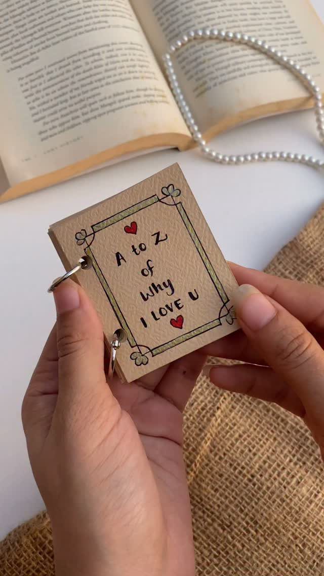 Handmade A to Z love booklet held by hands over an open book