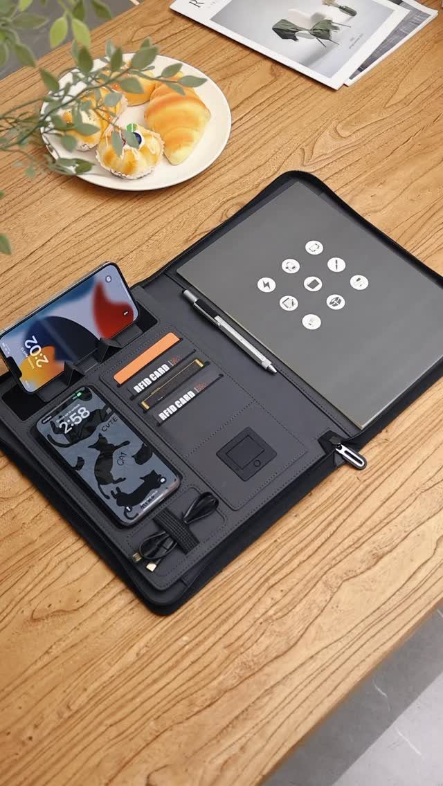 Black organizer portfolio with tablet and smartphones on a wooden table with pastries.