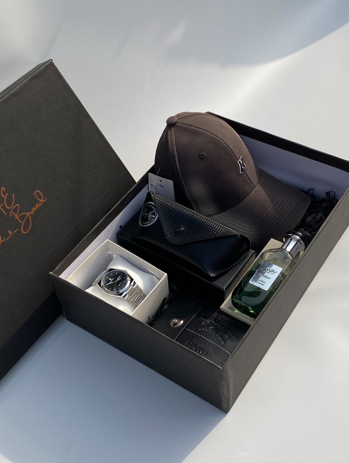 Gift box for men containing a watch, brown cap, wallet, cologne, and belt.