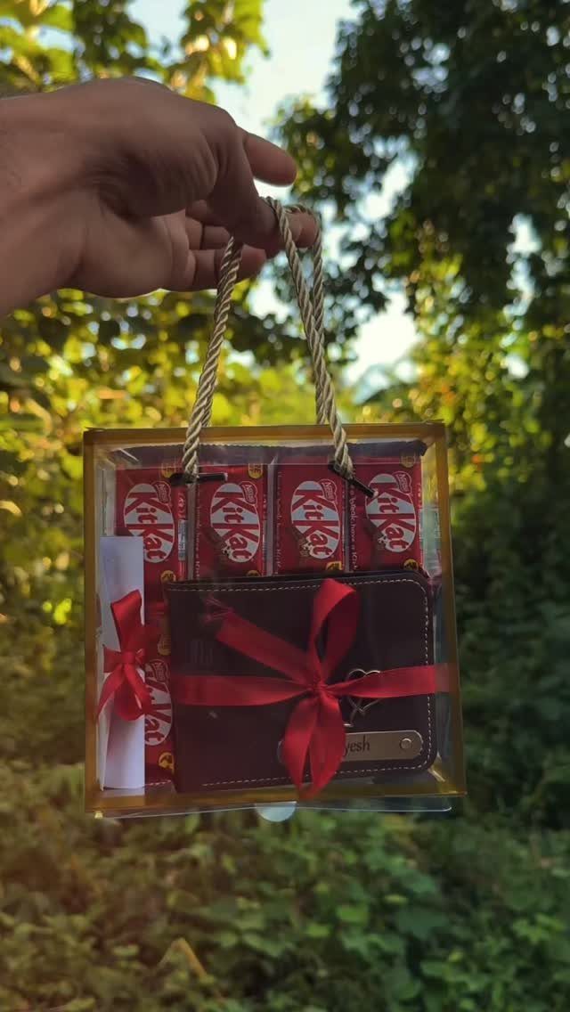 Gift box with a brown wallet, red ribbon, and KitKat chocolates outdoors.