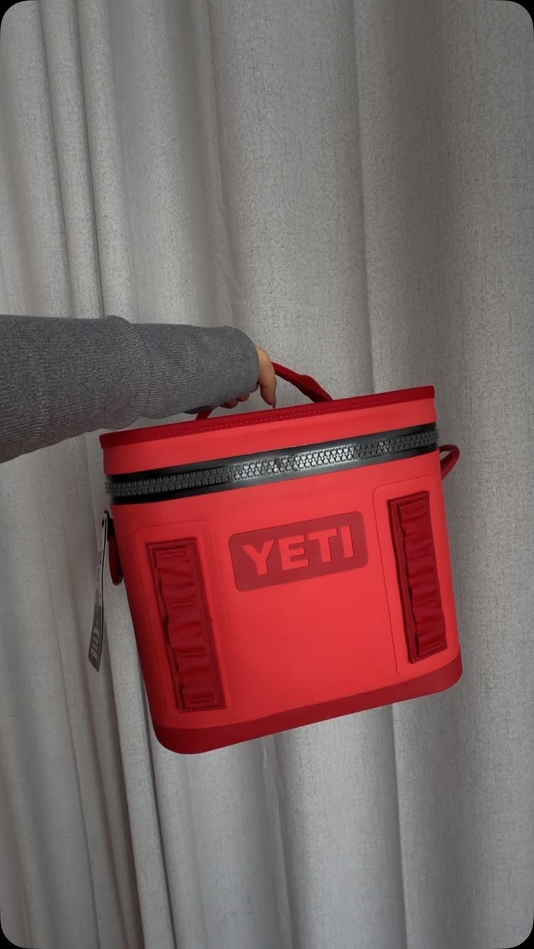 Red YETI Hopper Flip portable cooler bag held against a grey curtain background